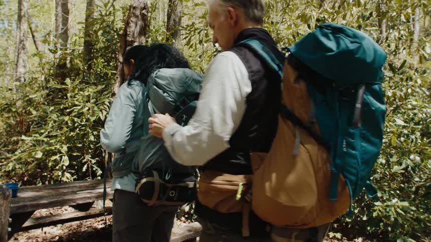 A man helps a woman by strapping her backpack