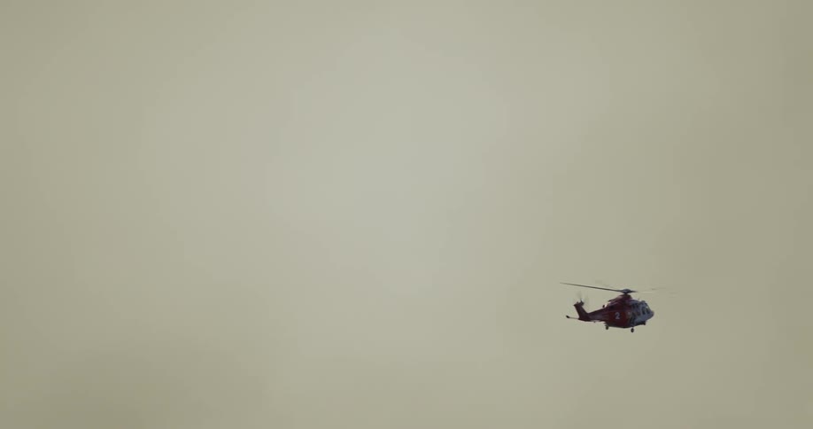 A helicopter flies in a hazy overcast sky its silhouette visible against the sky