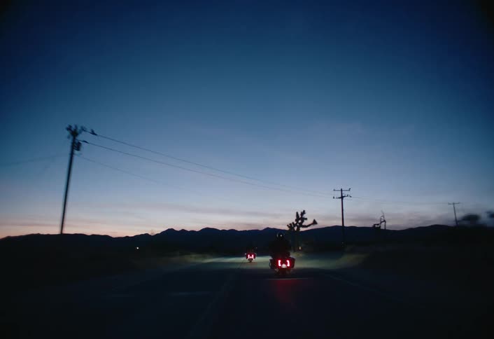 Motorcyclists ride their motorcycles along a rural highway near the mountains at night