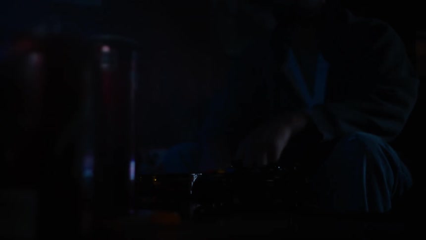 Closeup of a hand placing a video game controller on a coffee table with someone smoking or vaping nearby in a dark room