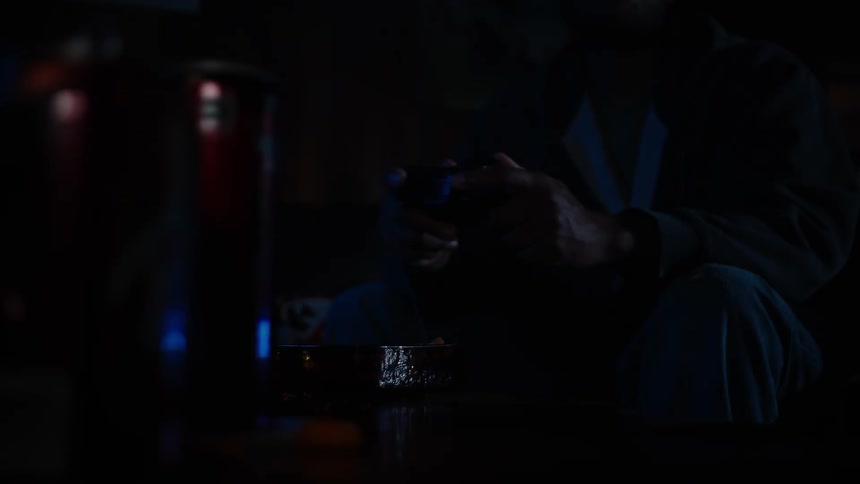 In the near darkness of a room someone is engrossed in playing a video game their controller illuminated by a faint light