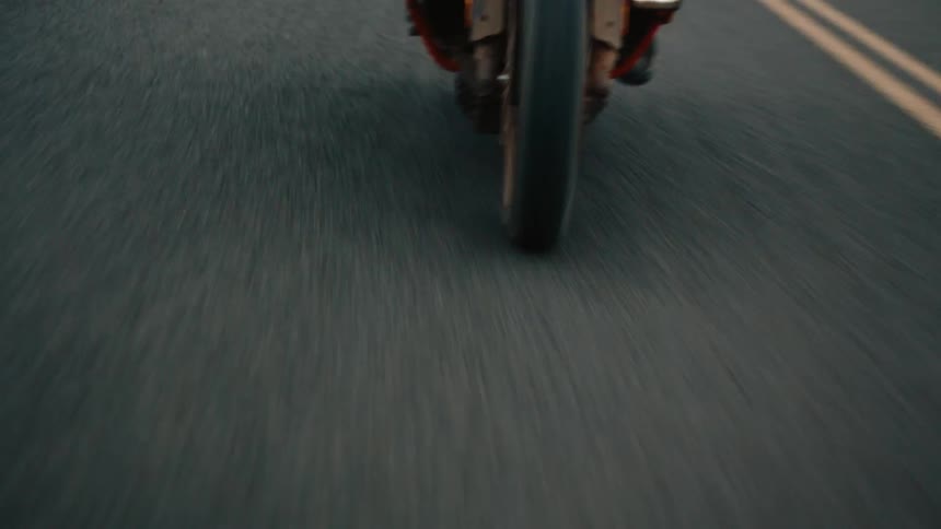 A motorcycle speeding down a gray asphalt road marked with solid yellow lines with a blurred desert landscape visible in the distance