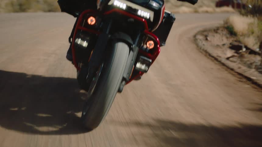 The front wheel and headlight of a motorcycle as it travels along a sandy desert like terrain