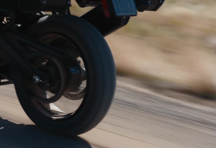 The rear wheel of a motorcycle speeds along a road in the terrain