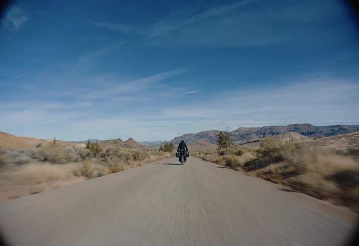 A motorcycle riding through the desert towards distant mountains