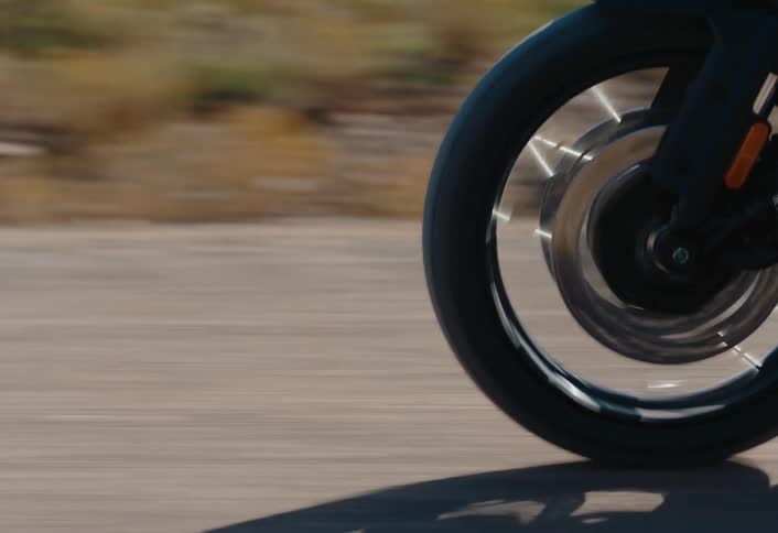 The rotating front wheel of a motorcycle showcasing the black rim silver brake disc and the motion blur of the asphalt road
