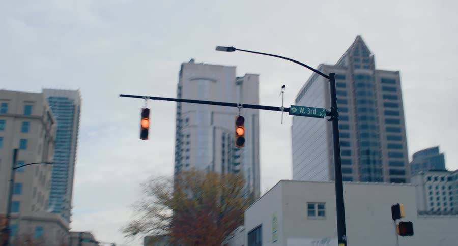 A deserted city street flanked by tall buildings and bare trees shows flashing traffic lights at an intersection