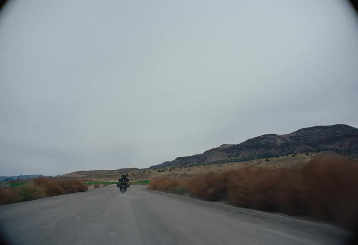 A person rides a motorcycle down the street in a desolate area surrounded by grassland