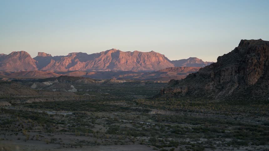 A wide landscape a rugged mountain range stretching across the horizon under a soft dusky sky with a dry rocky terrain in the foreground