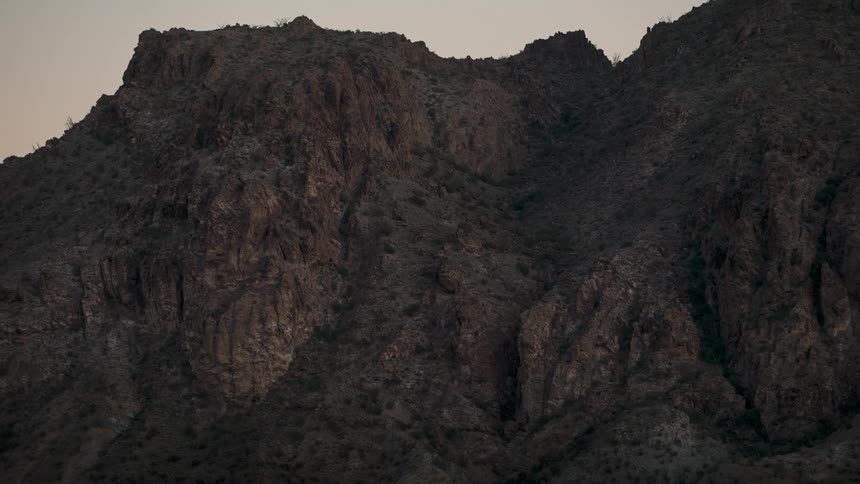 A dark silhouetted mountain range fills the frame under a dusky sky emphasizing the rugged texture and imposing presence of the natural landscape