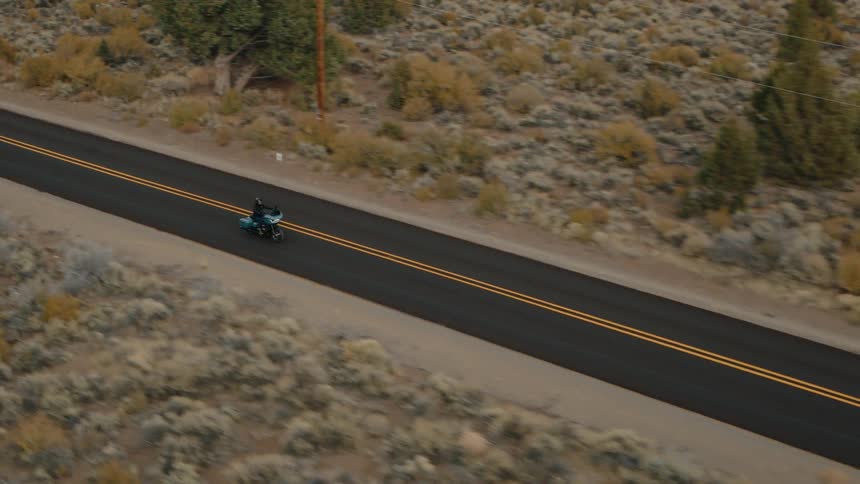 A motorcycle is driving on the highway past the trees and shrubland