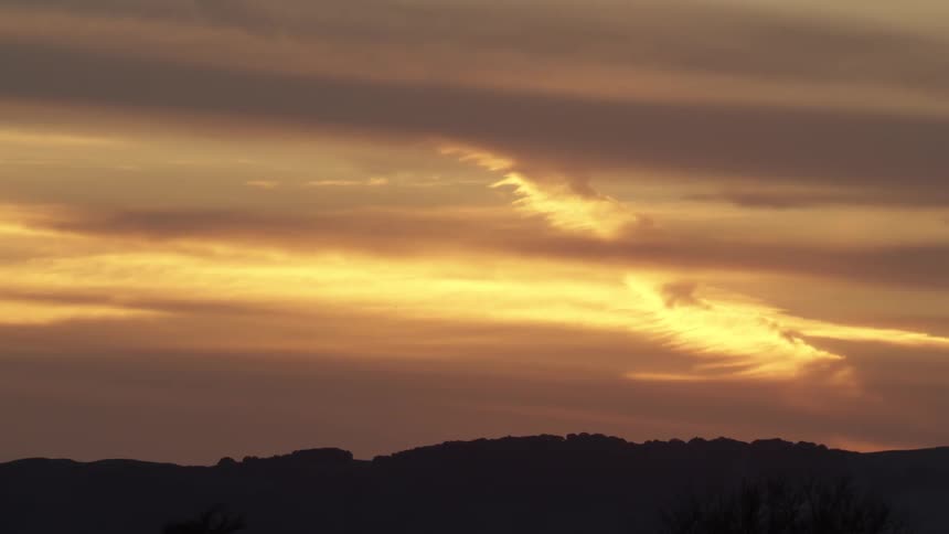 A dramatic sunset scene captures a dark silhouetted landscape against a vibrant sky filled with orange and yellow clouds