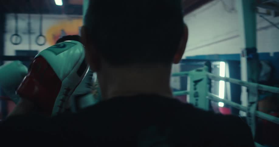 Female boxer practices with her trainer while in the boxing ring at a boxing gym