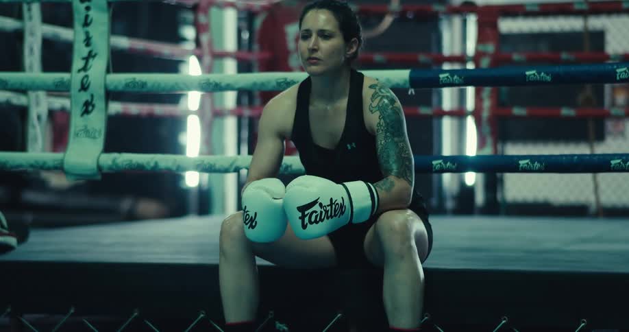 A woman is sitting down and resting while wearing boxing gloves