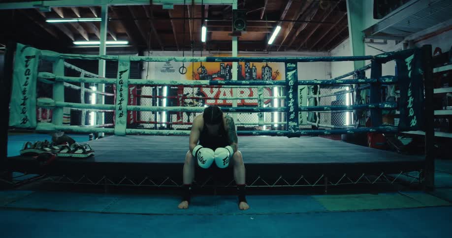 A resting women leans forward on the boxing ring