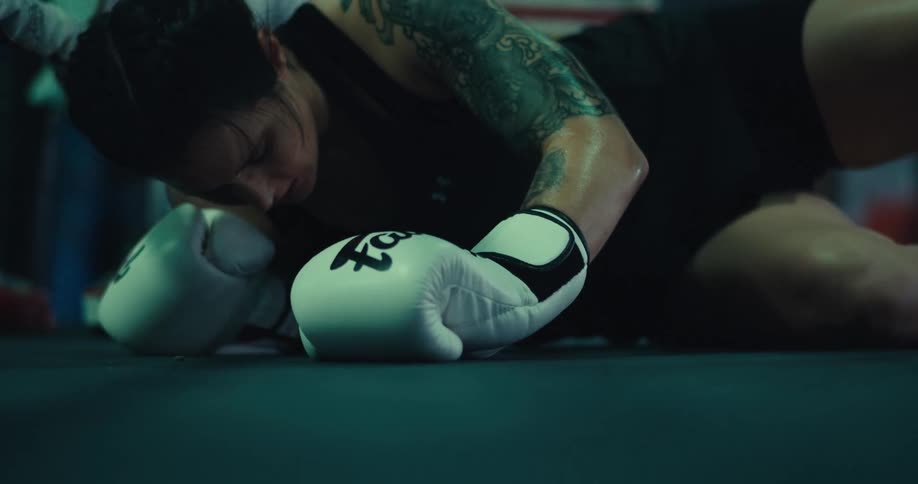 A female boxer falls down in a boxing ring while training