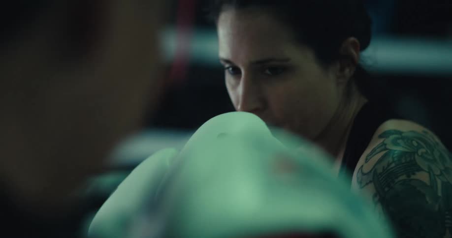 A woman is practicing boxing in a ring in a gym at night