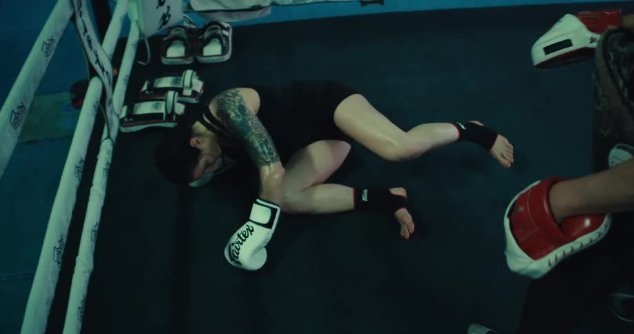Female boxer hits the floor after falling during a training session in the ring