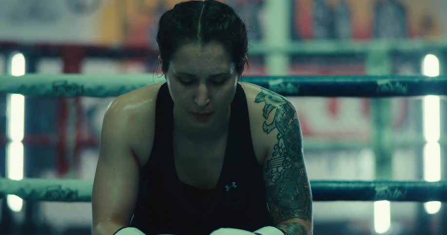 A woman punches her boxing gloves together by the ring