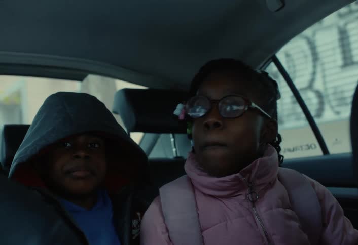 A boy and girl ride in the backseat of the car