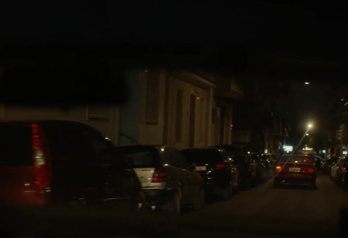 A car is driving along a city street at night surrounded by pedestrians and other vehicles