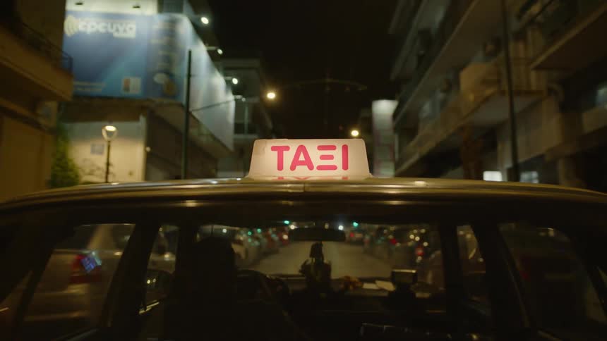 A view from the exterior of a moving taxi driving through the city at night
