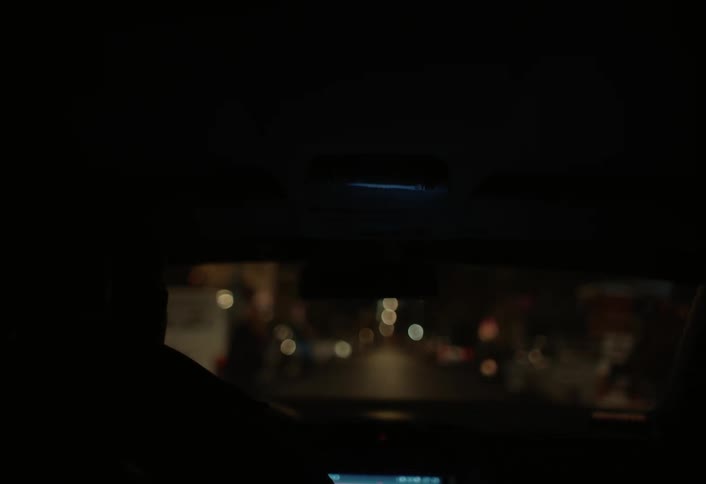 From inside a darkened vehicle blurred city lights are visible through the windshield at night