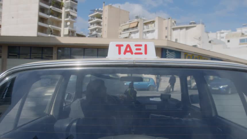 A view from the exterior of a moving taxi driving through the city under a clear blue sky