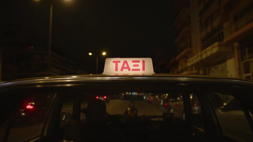 A car with a lit up taxi sign drives through a city at night