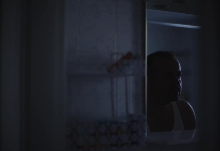 A dimly lit reflection in a mirror reveals a persons face and shoulder as they wash and clean themselves