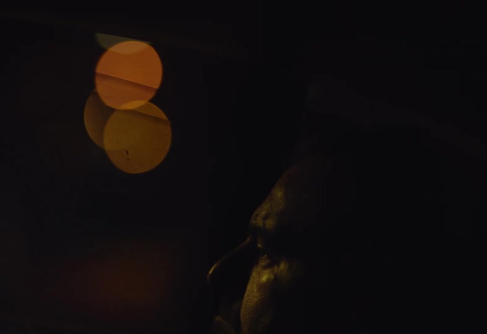 A closeup of a mans face as he sits in a dimly lit car while the glow of passing headlights illuminates the scene intermittently