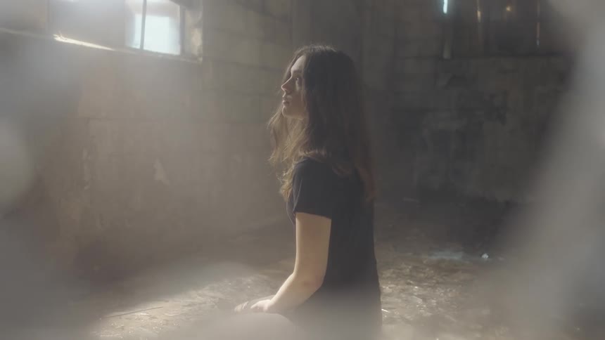 A woman kneels on the floor and looks up towards a sunny window