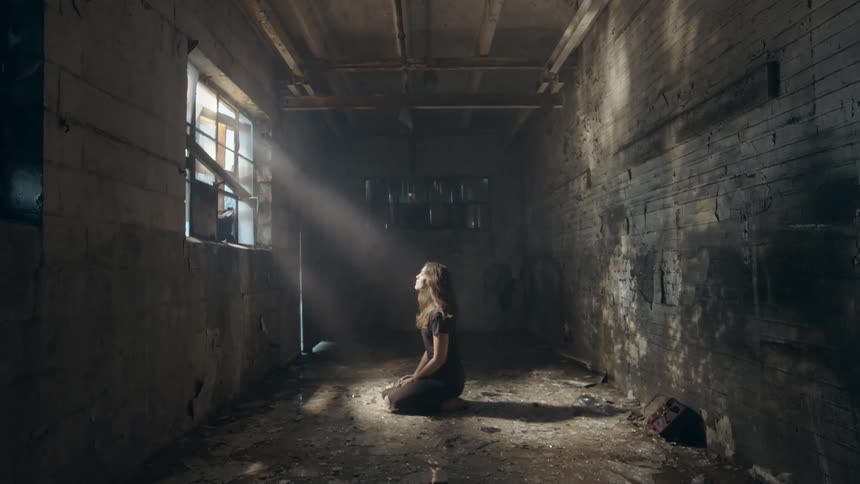 A woman on her knees in a building looking up at a window where the sun is shining through
