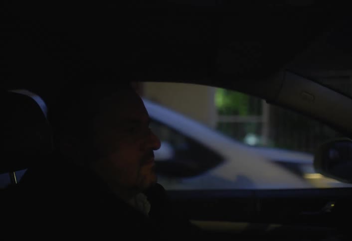 A man gets into his car and drives at night
