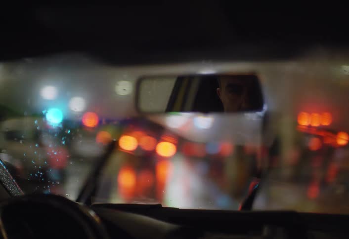 Rain streaks a vehicles windshield as windshield wipers move across it while driving on the city at night