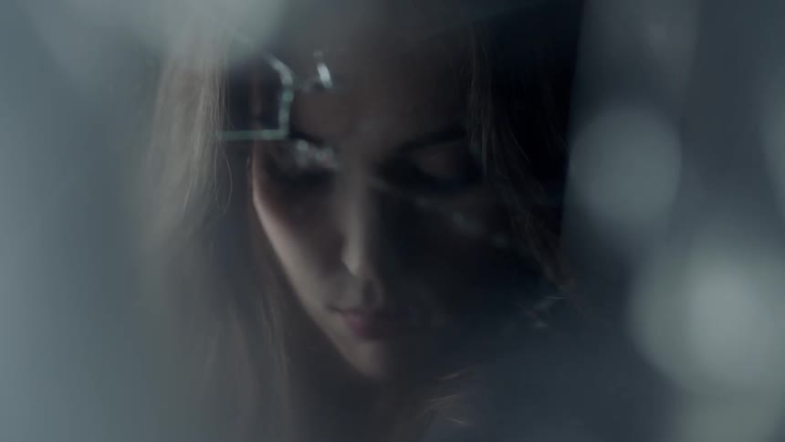 A woman is looking down in front of a cracked mirror