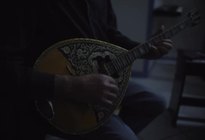 A person is playing a bouzouki a stringed instrument with a pear shaped body and a long neck in a dimly lit setting