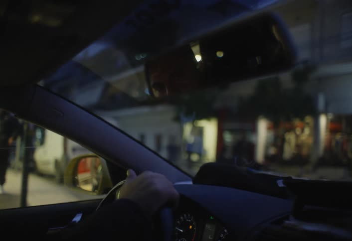 A man looks into the rearview mirror as he drives at night