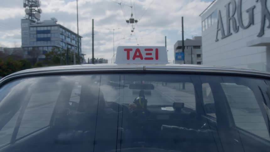 A view from the exterior of a moving taxi driving through the city under a cloudy sky