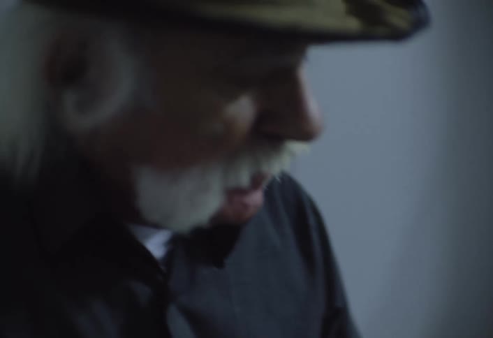 A man with a hat and a mustache plays a bouzouki with the focus on his fingers moving along the fretboard and the decorative inlays of the instrument
