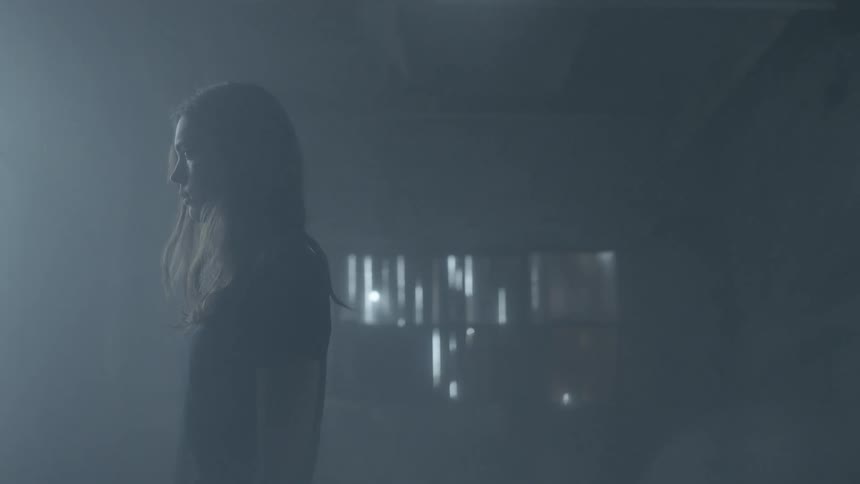 A woman stands alone in a room with her eyes closed