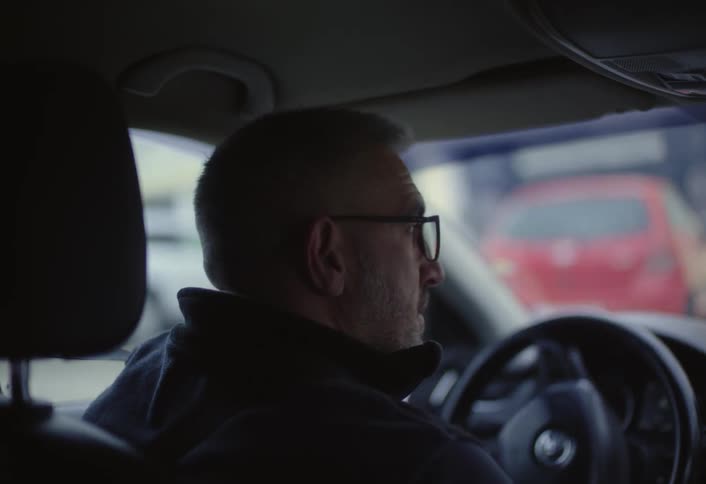 A man with short gray hair is seen from behind driving a car
