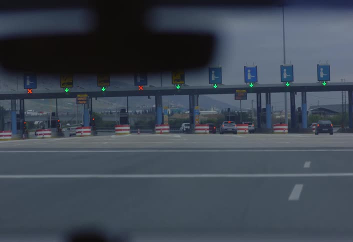 A view from inside a vehicle shows a toll plaza with multiple lanes and a few cars passing through