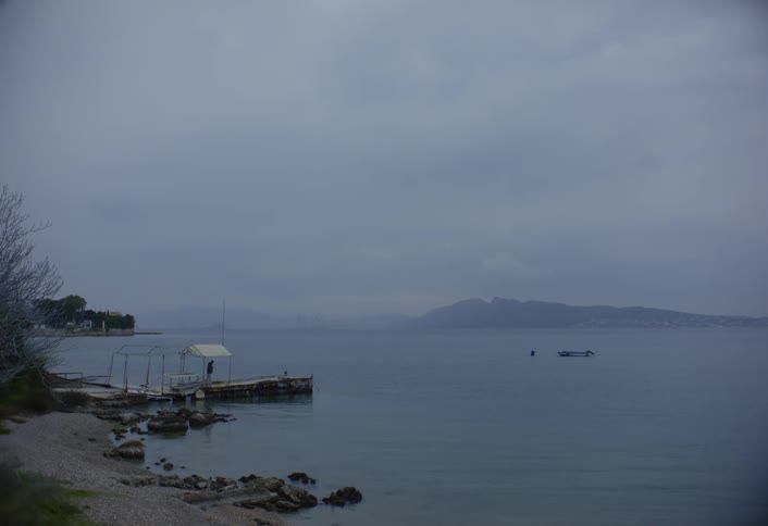 A man walks to the end of a pier looking at a boat in the lake