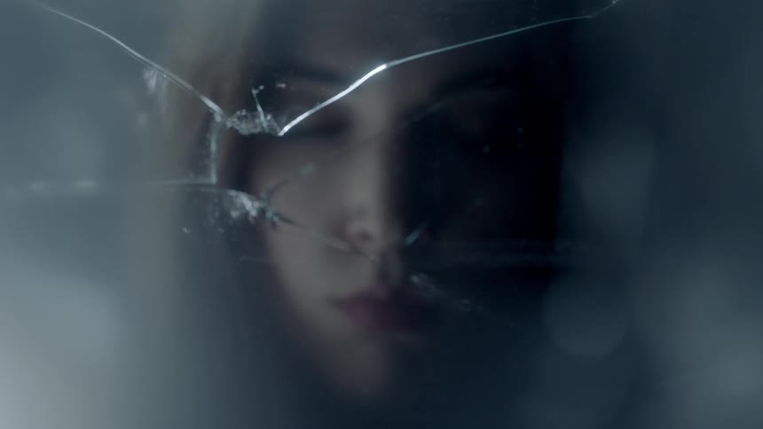 A woman has her eyes closed in front of broken glass before opening them