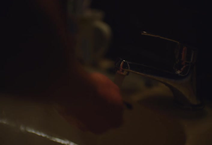 A man washing his hands under running water from a faucet in a dimly lit bathroom