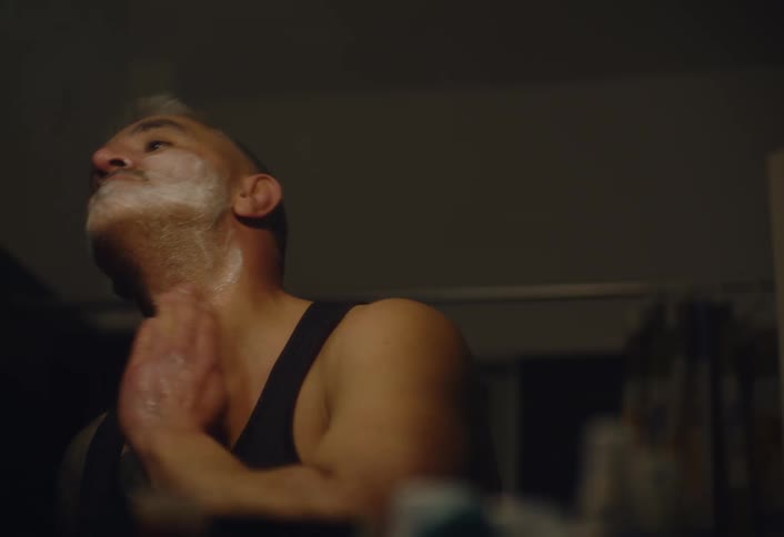 A man with short light colored hair and facial hair applying shaving cream in the bathroom