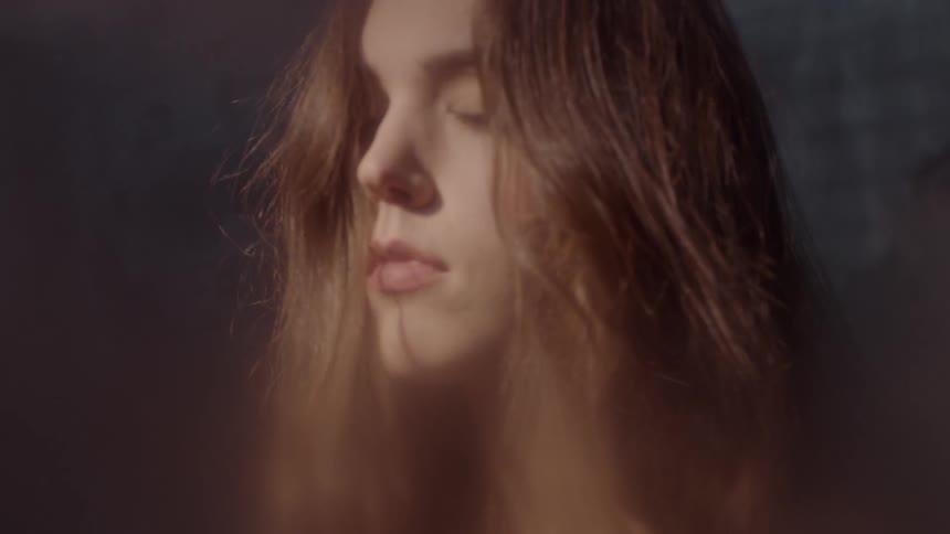 A woman's face slowly lights up in a dark room