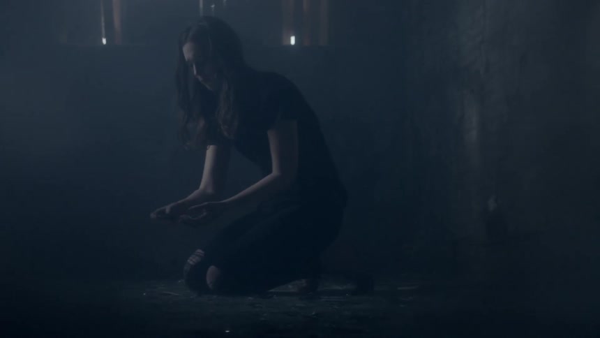 A woman kneels on the ground and picks up shards of glass