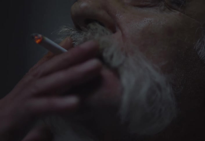 An elderly man with white hair and beard smoking a cigarette and exhaling smoke